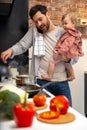 Multitasking father babysitting, cooking breakfast and talking on smart phone at home. Royalty Free Stock Photo