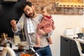 Multitasking father babysitting, cooking breakfast and talking on smart phone at home. Royalty Free Stock Photo