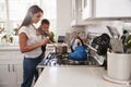 Multitasking mum holding her young baby while she makes food at the hob in her kitchen, side view Royalty Free Stock Photo