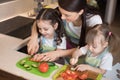 Mum chopping vegetables with kids daughters in a family home kitchen. Royalty Free Stock Photo
