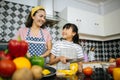 Mum and her daughter help each other to preparing cooking in kitchen at home.