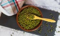 Mung beans in a clay bowl with a wooden spoon on a slate board on a marble countertop