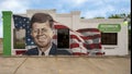 Mural by Art Velazquez featuring JFK with an American flag in the background on the wall of Greenhouse Smoke & Vapes in Grand Prai