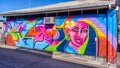 Mural graffiti wall art of a colourful lady with flower in car park area