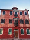 Murano, Italy - February 2019: Beautiful red house building with green windows details on wood, typical construction in Murano