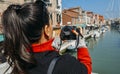 Young brunette woman takes a picture of a colorful canal in Murano with a DSLR camera