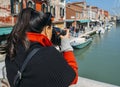 Young brunette woman takes a picture of a colorful canal in Murano with a DSLR camera