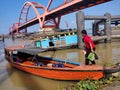 Murky river with bridge, people, boats, plants, trees and blue sky background