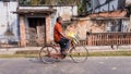 An Indian man riding a bicycle past a rustic house in the old town of Murshidabad