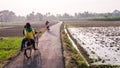 Kids riding a bicycle through a narrow country road passing through green fields