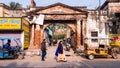 People walking past the ruins of an ancient arched brick gateway in the old town
