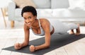 Muscle strengthening exercises. Happy African American woman doing elbow plank, training on yoga mat at home Royalty Free Stock Photo