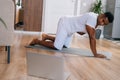 African-American man doing workout with online trainer using laptop at home standing in side plank. Royalty Free Stock Photo