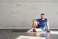 Muscular athlete sitting in sunny sport club, relaxed after workout, bottle of water in hands. Space for text layout on brick wall