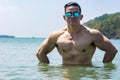 A muscular and athletic asian man wearing shades takes a dip in the sea. Summertime body goals for the beach Royalty Free Stock Photo