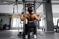 Muscular athletic female bodybuilder in black suit pulled on sports simulator in gym. Back muscles are very tense
