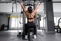 Muscular athletic female bodybuilder in black suit pulled on sports simulator in gym. Back muscles are very tense