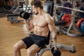 Muscular athletic young man bodybuilder fitness model exercise biceps with dumbbell on the bench in gym. Royalty Free Stock Photo