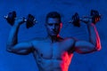 Muscular bodybuilder man exercising with dumbbells in colorful neon light Royalty Free Stock Photo