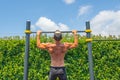 Muscular caucasian man in a cap doing pull-ups on the horizontal bar in the park outdoors, rear view of his back Royalty Free Stock Photo