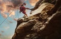 Muscular climber man in protective helmet abseiling from cliff rock wall using rope Belay device and climbing harness on evening