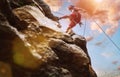 Muscular climber man in protective helmet abseiling from cliff rock wall using rope Belay device and climbing harness on evening