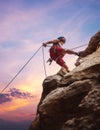 Muscular climber man in protective helmet abseiling from cliff rock wall using rope Belay device and climbing harness on evening