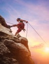 Muscular climber man in protective helmet abseiling from cliff rock wall using rope Belay device and climbing harness on evening