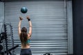 Woman tossing medicine ball against roll-up door in gym garage with weight rack, bench Royalty Free Stock Photo
