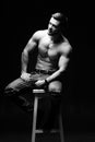 Muscular and fit young bodybuilder fitness male model posing on chair. Black and white photo. Full size portrait. Royalty Free Stock Photo