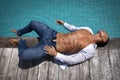 Muscular gorgeous sexy young wet man with athletic body is lies next to the pool on a wooden platform in blue jeans and white Royalty Free Stock Photo