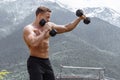 Muscular male athlete with arms raised doing lifting exercises dumbbells.