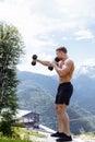 Muscular male athlete with arms raised doing lifting exercises dumbbells.