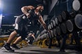 Muscular male in black shorts, vest, cap. Exercising with dumbbells for training his triceps, leaning on set of black Royalty Free Stock Photo