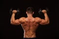 Muscular male model bodybuilder doing exercises with dumbbells, turned back. Isolated on black background with copyspace Royalty Free Stock Photo