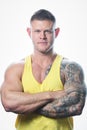 Muscular man with blue eyes and tattoo in the yellow tank top on the white background in a gym Royalty Free Stock Photo