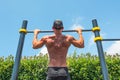 Muscular man in a cap doing pull-ups on the horizontal bar in the park outdoors, back view of his back Royalty Free Stock Photo
