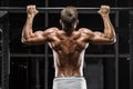 Muscular man doing pull up on horizontal bar in gym, working out. Strong fitness male showing back