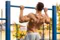 Muscular man doing pull up on horizontal bar, working out. Strong fitness male pulling up, showing back, outdoors