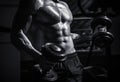 Muscular man on gym background with dumbbell. Athlete in the gym training with dumbbells. Abs and biceps. Muscular man