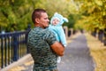 A muscular man holds the baby in warm jumpsuit in the fall on a walk. yellow leaves