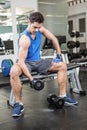 Muscular man lifting dumbbell while sitting on bench Royalty Free Stock Photo