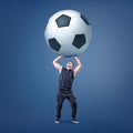 A muscular man tries to hold a giant and heavy black and white football ball over himself. Royalty Free Stock Photo