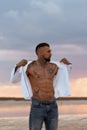 Muscular sexy young man taking off t shirt on empty white sand beach and turquoise ocean Royalty Free Stock Photo