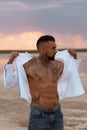 Muscular sexy young man taking off t shirt on empty white sand beach and turquoise ocean Royalty Free Stock Photo