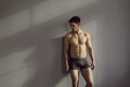 Muscular shirtless male model in underwear posing in sensual pose against gray wall background.
