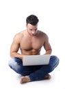 Muscular, shirtless young man on the floor using laptop computer