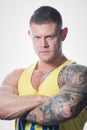 Muscular strong man with blue eyes and tattoo in the yellow tank top on the white background in a gym Royalty Free Stock Photo