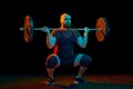 Muscular, strong young man, bodybuilder doing squats and lifting barbell, heavy weights over black background in neon Royalty Free Stock Photo