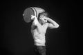 Muscular worker shirtless holding big blue barrel over his head.